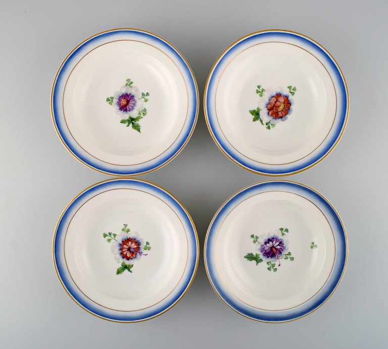 Four antique Royal Copenhagen deep plates in hand-painted porcelain with flowers and blue edge with gold. Model number 592/9050. Late 19th century.