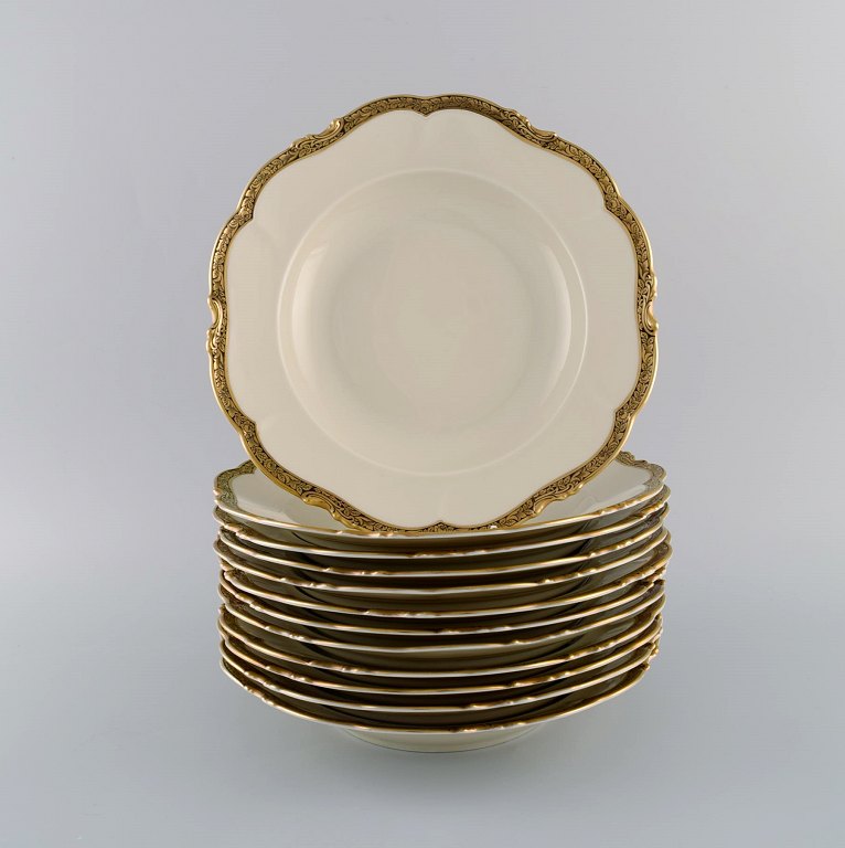 KPM, Berlin. Tolv Royal Ivory dybe tallerkener i cremefarvet porcelæn med 
gulddekoration. 1920