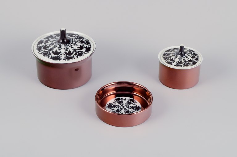 Bjørn Wiinblad for Rosenthal, Tyskland. ”Berlin Hilton”. To lågkrukker og en 
flaskebakke i porcelæn. Glansfuld kobberfarvet