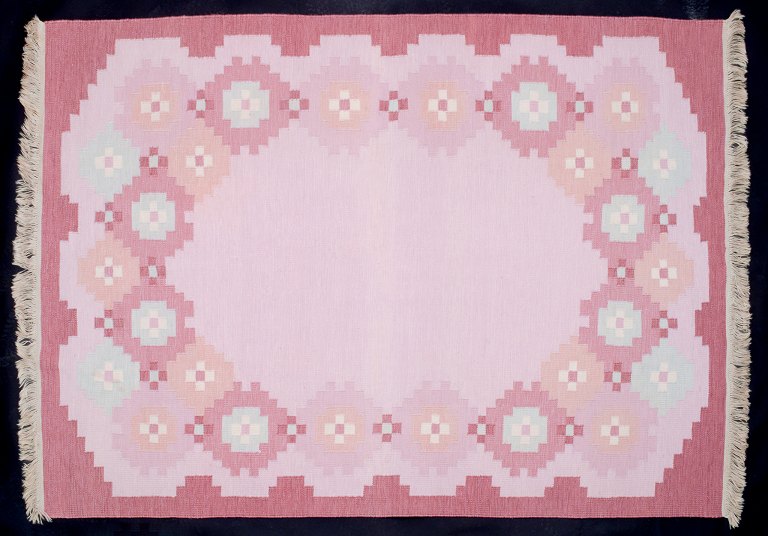 Svensk tekstilkunstner. Stort håndvævet uldtæppe i Rölakan-teknik. Modernistisk 
design. Lyserøde, røde og blå farver i geometrisk mønster.