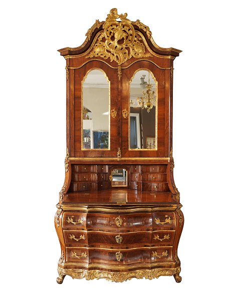 Pragtchatol udført i Mathias Ortmann manér. Nøddetræ m. forgyldninger prydet med talrige skæringer. Overskab med spejlglas i låger bag hvilke hylder. Skriveplade med trappeformede skuffer og låge med spejl. Bombéformet underdel. H: 276cm. B: 137cm. D: 100